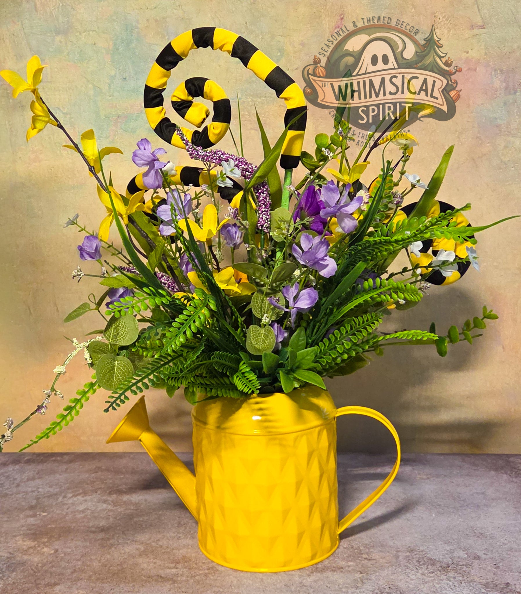 Yellow watering can filled with flowers on a textured surface, with 'Whimsical Spirit' branding in the background.