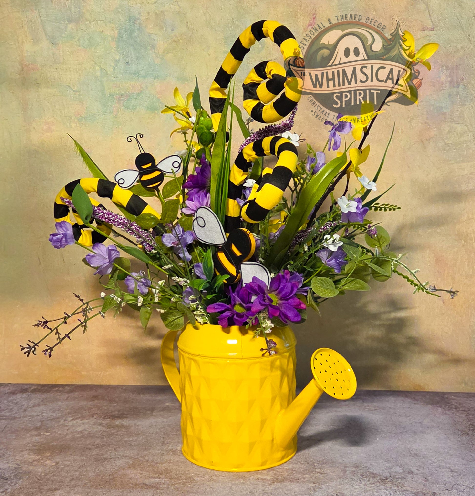 Decorative arrangement with flowers, bees, and a yellow watering can on a textured surface.