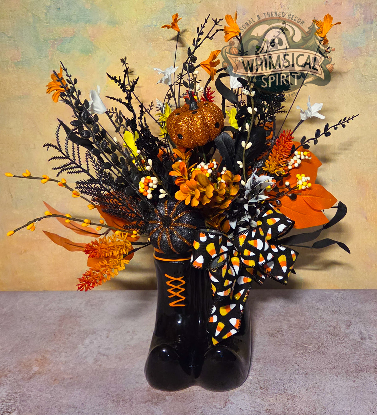 Halloween witch boots centerpiece with glitter pumpkins, black foliage, orange flowers, candy-colored berries, and a candy corn bow.
