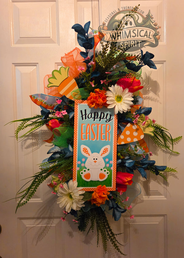 Decorative Easter wreath with flowers and a sign on a white door.