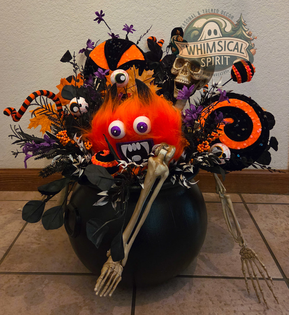 Cauldron of Chaos handmade Halloween centerpiece in a black cauldron with orange monster, skeleton, eyeballs, purple florals, and black-and-orange accents.