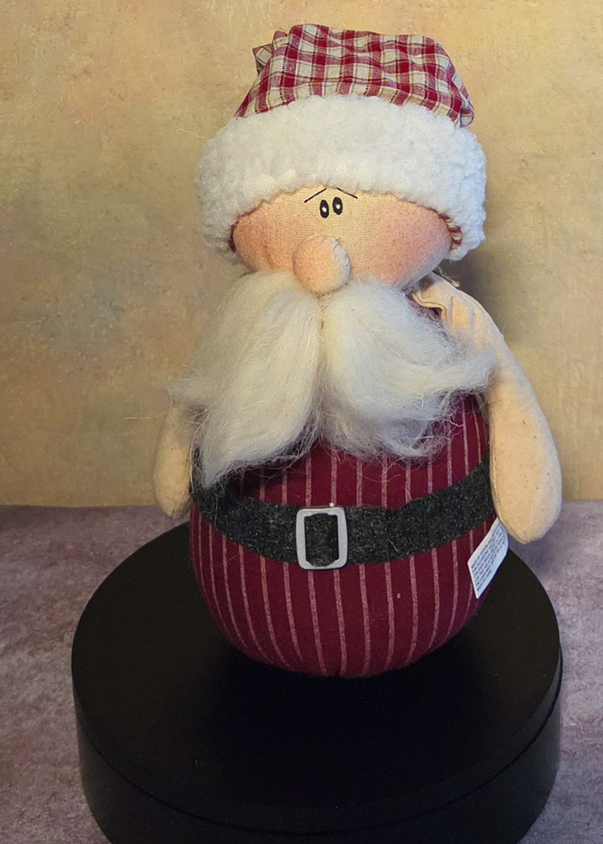 Front view of Claus Santa soft sculpture with a red plaid hat, fluffy white mustache and beard, black belt, silver buckle, and dark feet.