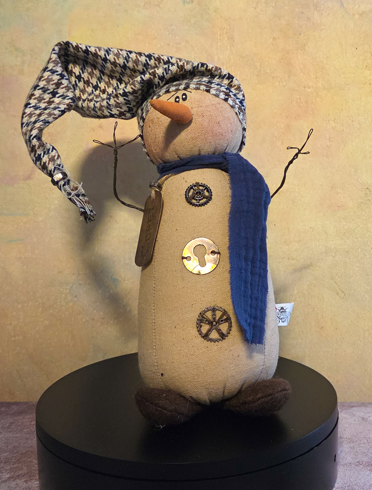 Corey the Snowman winter soft sculpture shelf sitter with floppy patterned hat, blue scarf, twig arms, carrot nose, and button details.