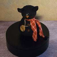 Front view of Ebony black cat soft sculpture with pointed ears, orange plaid scarf, rustic bell buttons, and wooden name tag.