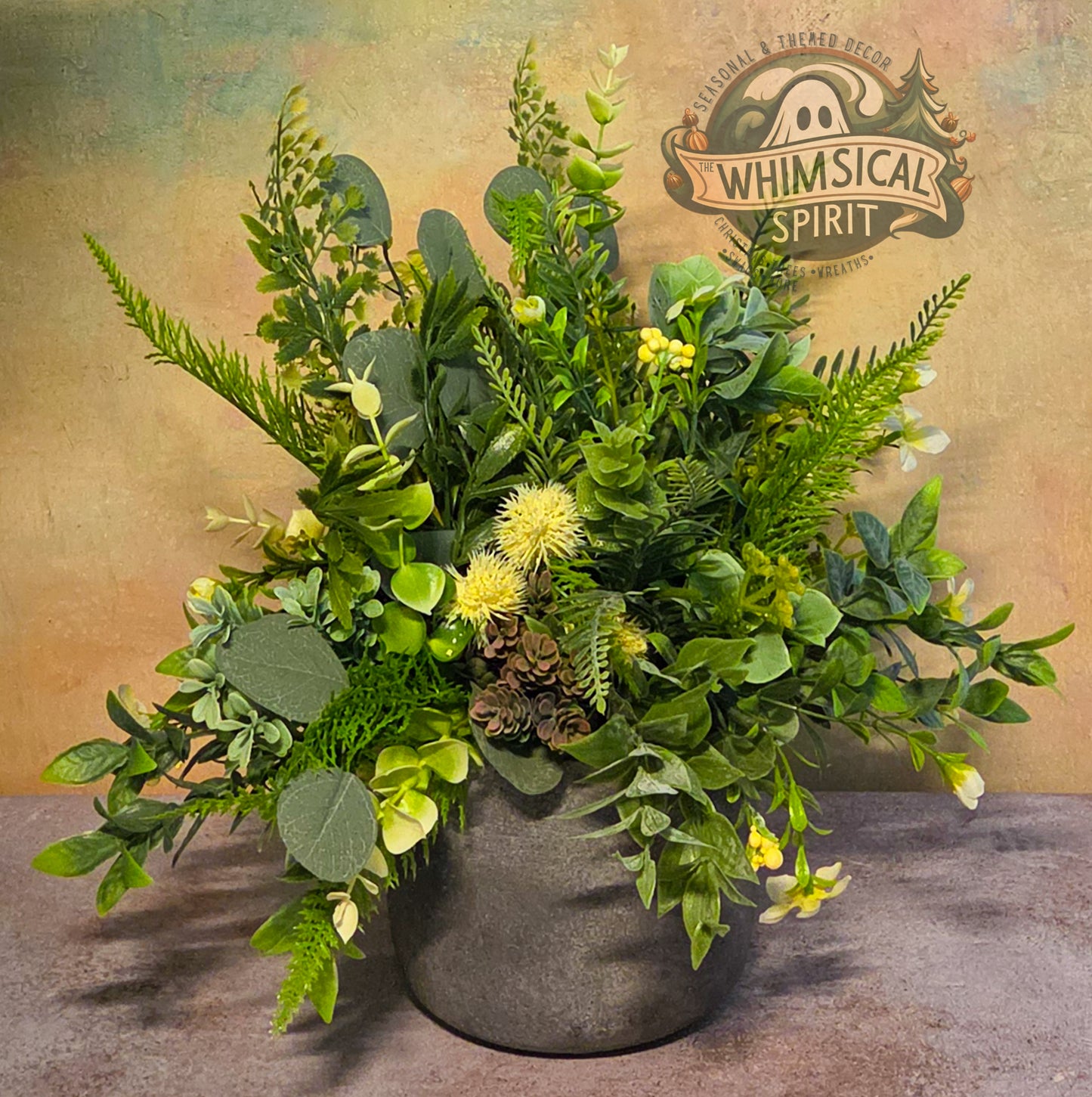 Artificial greenery arrangement in a pot with 'Whimsical Spirit' branding in the background.