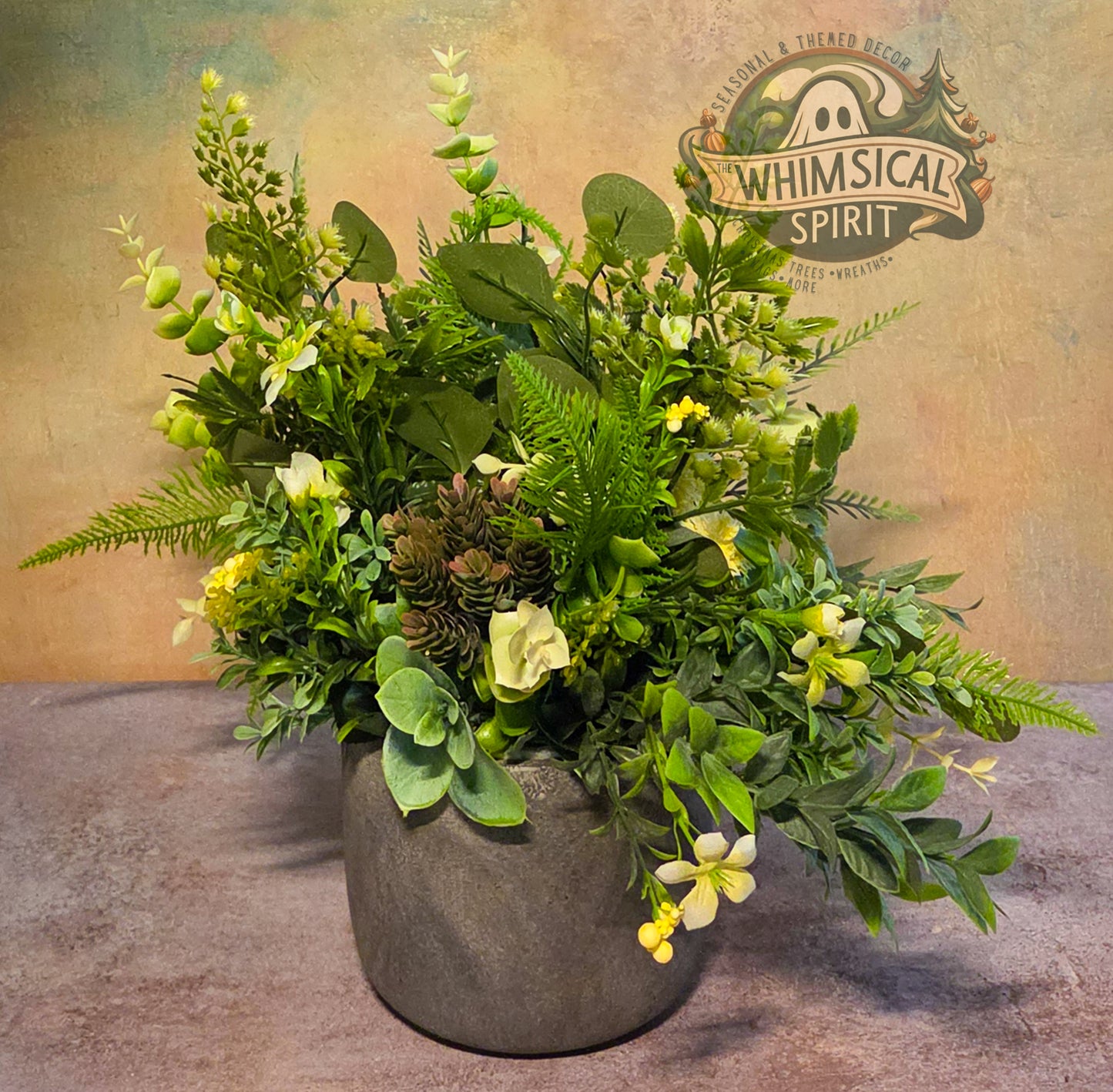 Artificial greenery arrangement in a pot with 'Whimsical Spirit' branding on a textured background