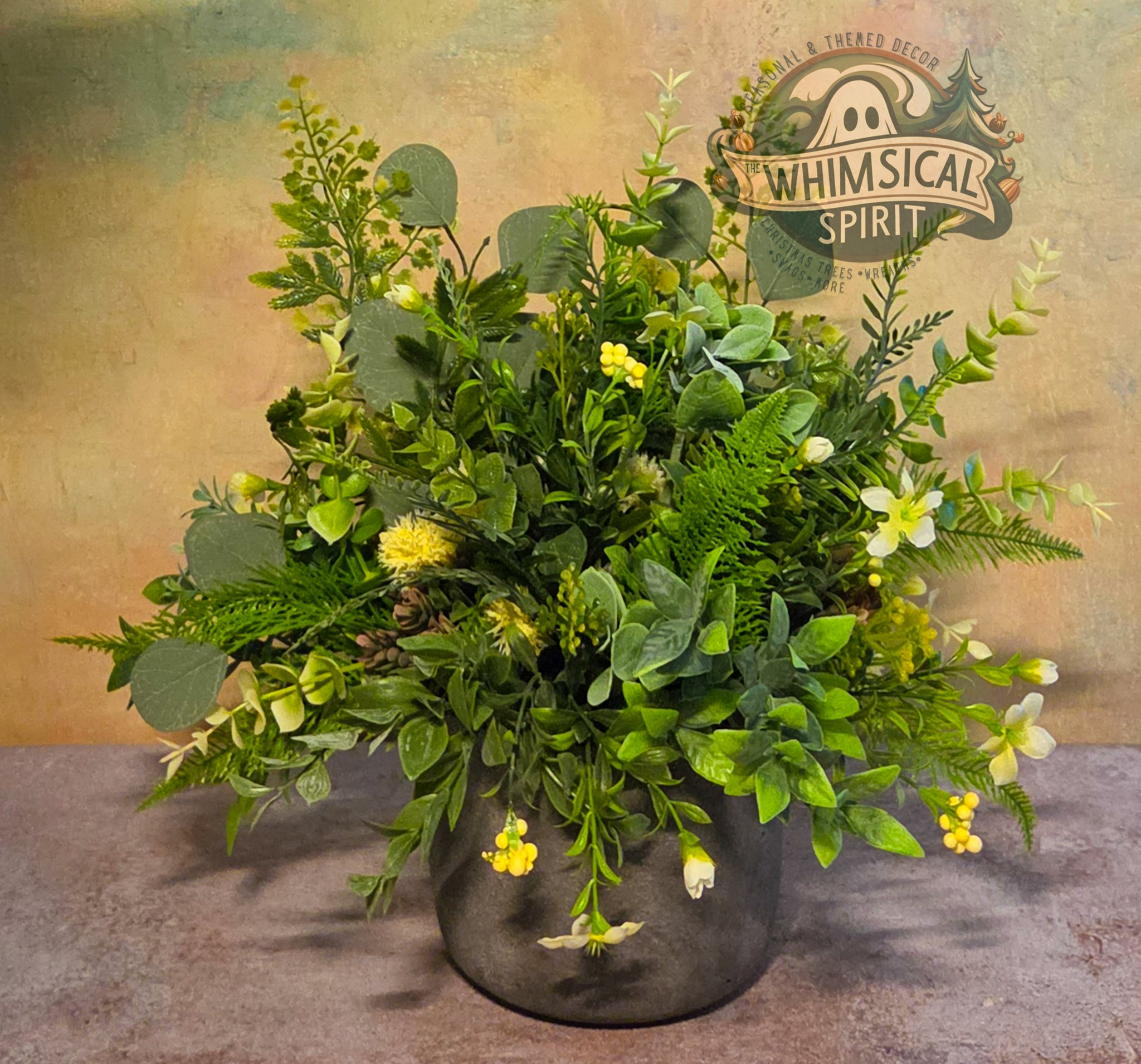 Faux greenery arrangement in a pot with 'Whimsical Spirit' branding on a textured background