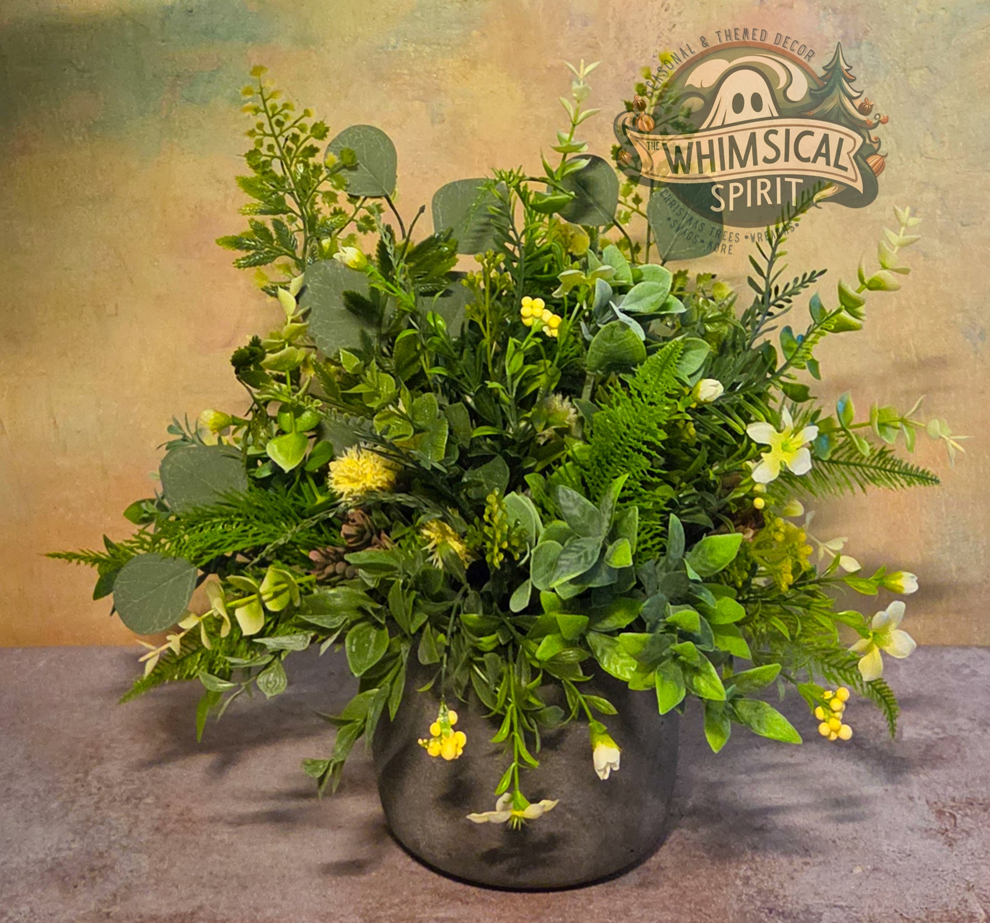 Faux greenery arrangement in a pot with 'Whimsical Spirit' branding on a textured background