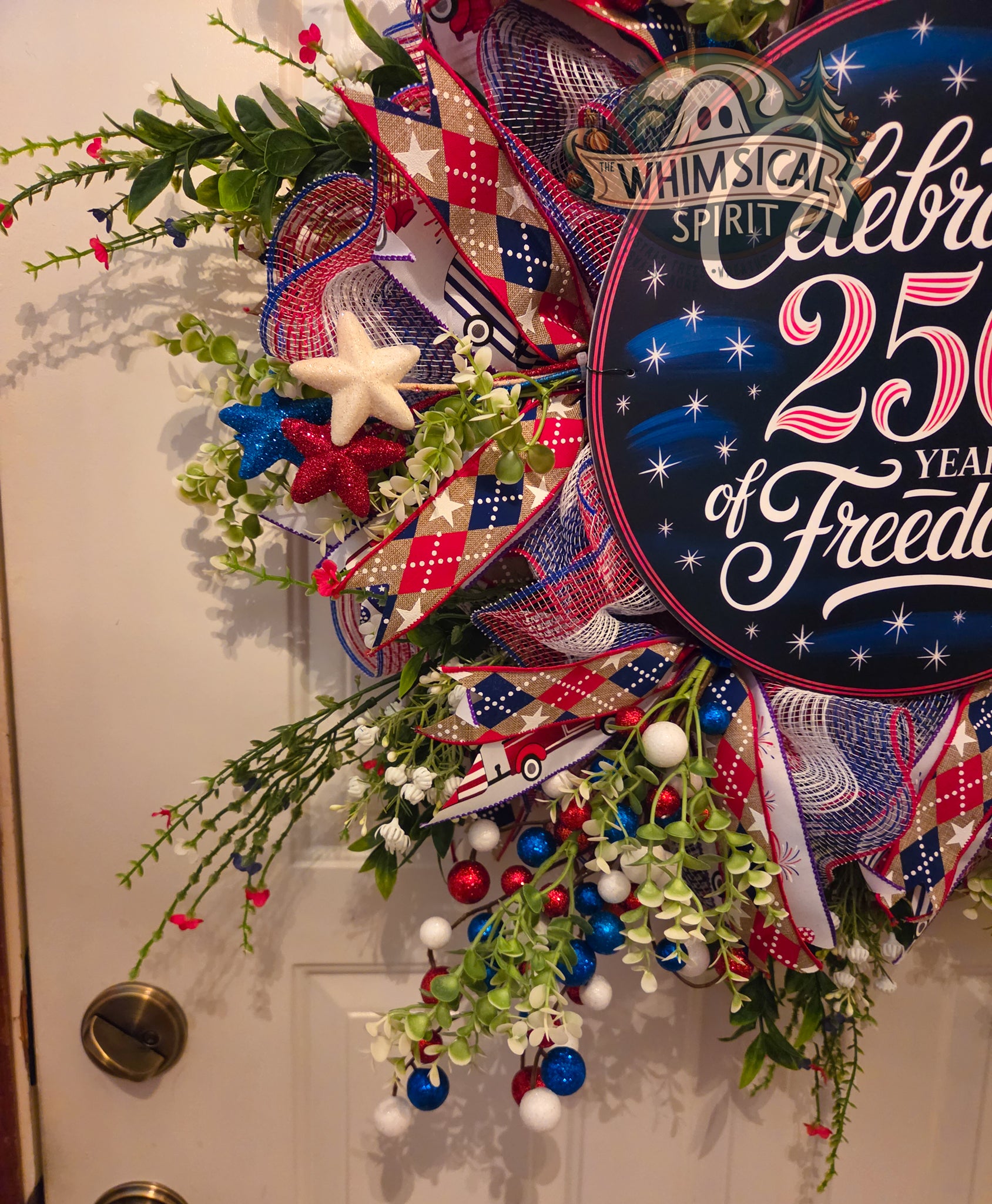 Decorative wreath with American flag elements and 'Whimsical Spirit' sign on a door.