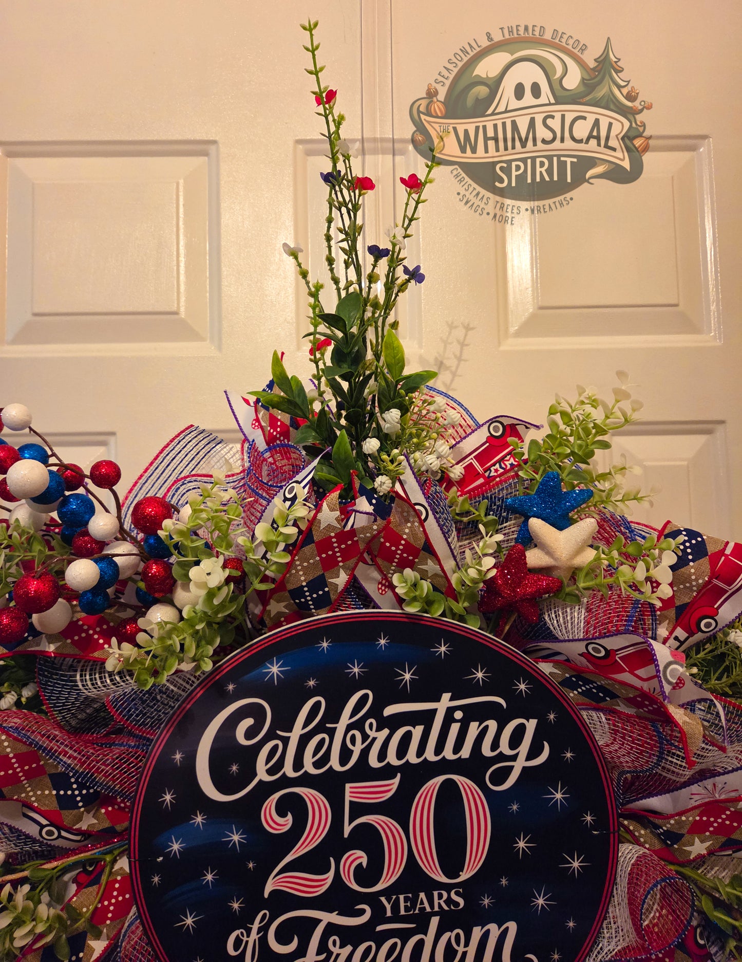 Decorative wreath with red, white, and blue elements and a sign celebrating 250 years of freedom in front of a door with 'Whimsical Spirit' decor.