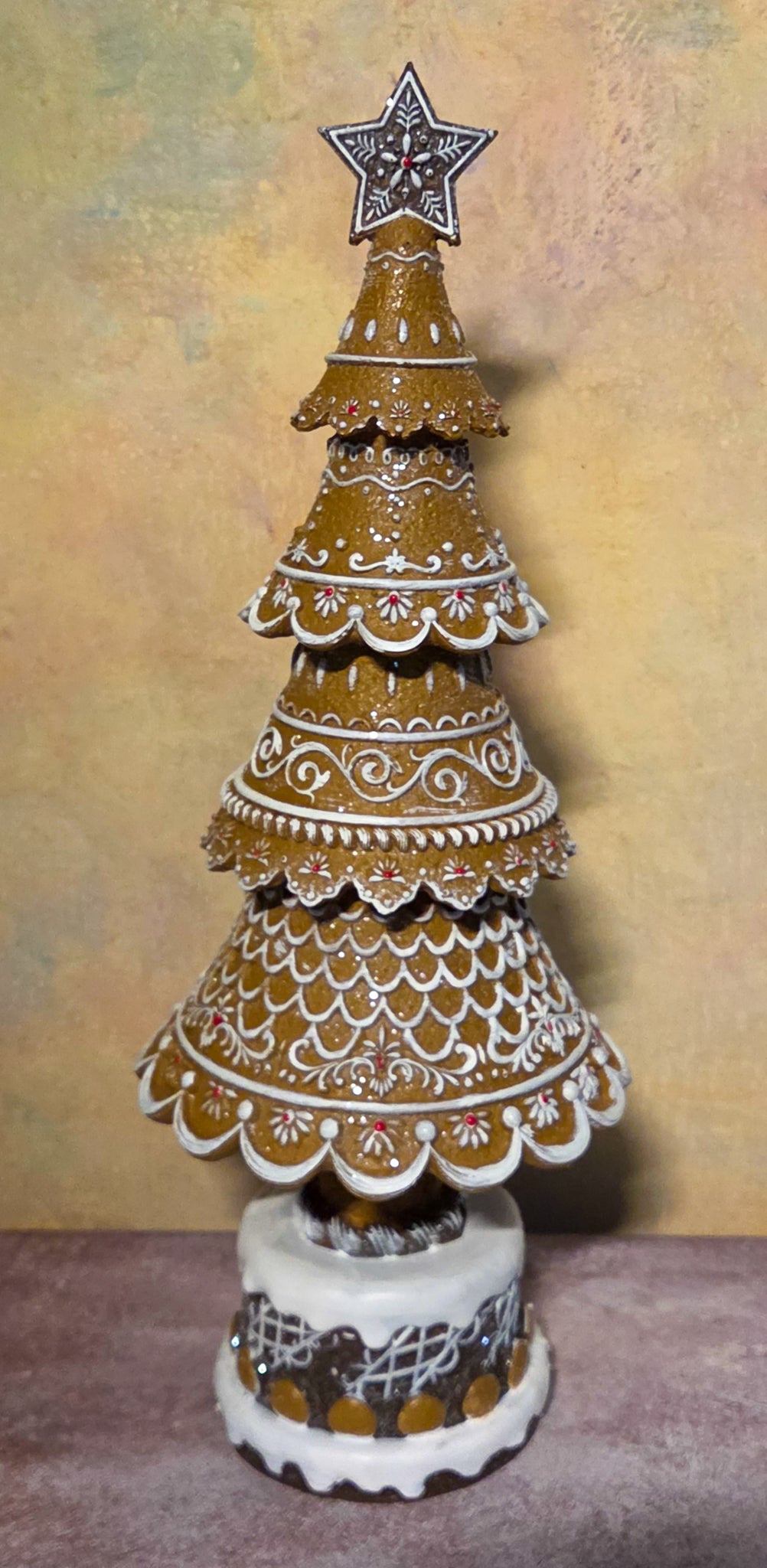 Large tiered gingerbread Christmas tree decorated with ornate white icing patterns, small red accents, a star topper, and a snowy base.