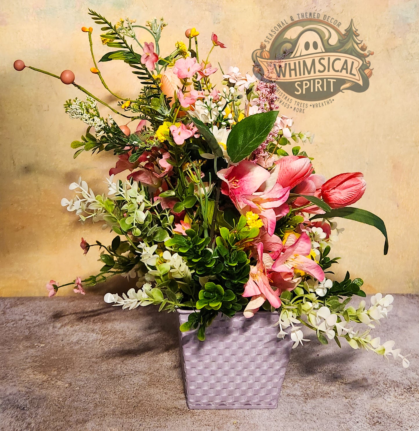 Floral arrangement in a woven basket with 'Whimsical Spirit' logo in the background
