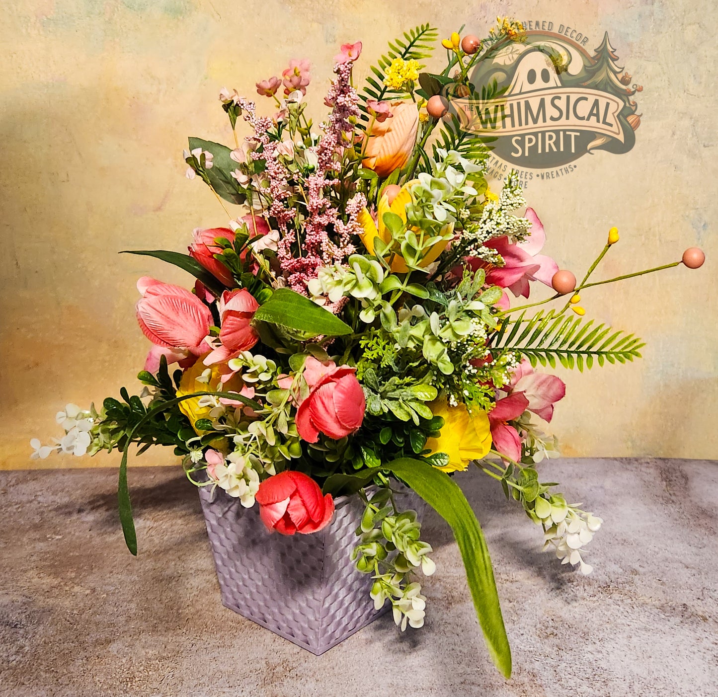 Colorful flower arrangement in a gray basket with 'Whimsical Spirit' branding in the background.