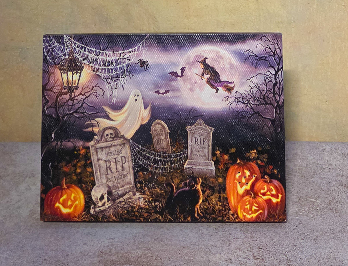 Graveyard Glow light-up Halloween tabletop canvas featuring a ghost, witch, gravestones, bats, black cat, cobwebs, and jack-o’-lanterns.