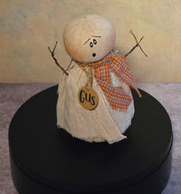 Front view of Gus ghost soft sculpture with distressed cream fabric, twig arms, orange plaid scarf, expressive face, and wooden name tag.