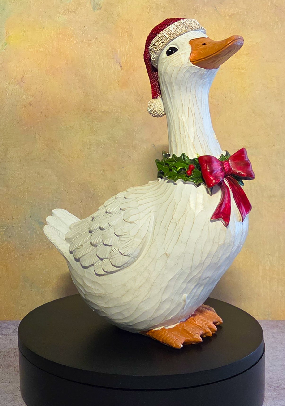 White Christmas goose resin figurine wearing a red Santa hat and holly collar with red bow, shown as tabletop holiday decor.