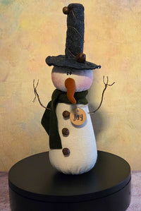 Jay the Snowman winter soft sculpture shelf sitter with tall black hat, green scarf, twig arms, carrot nose, button details, and name tag.