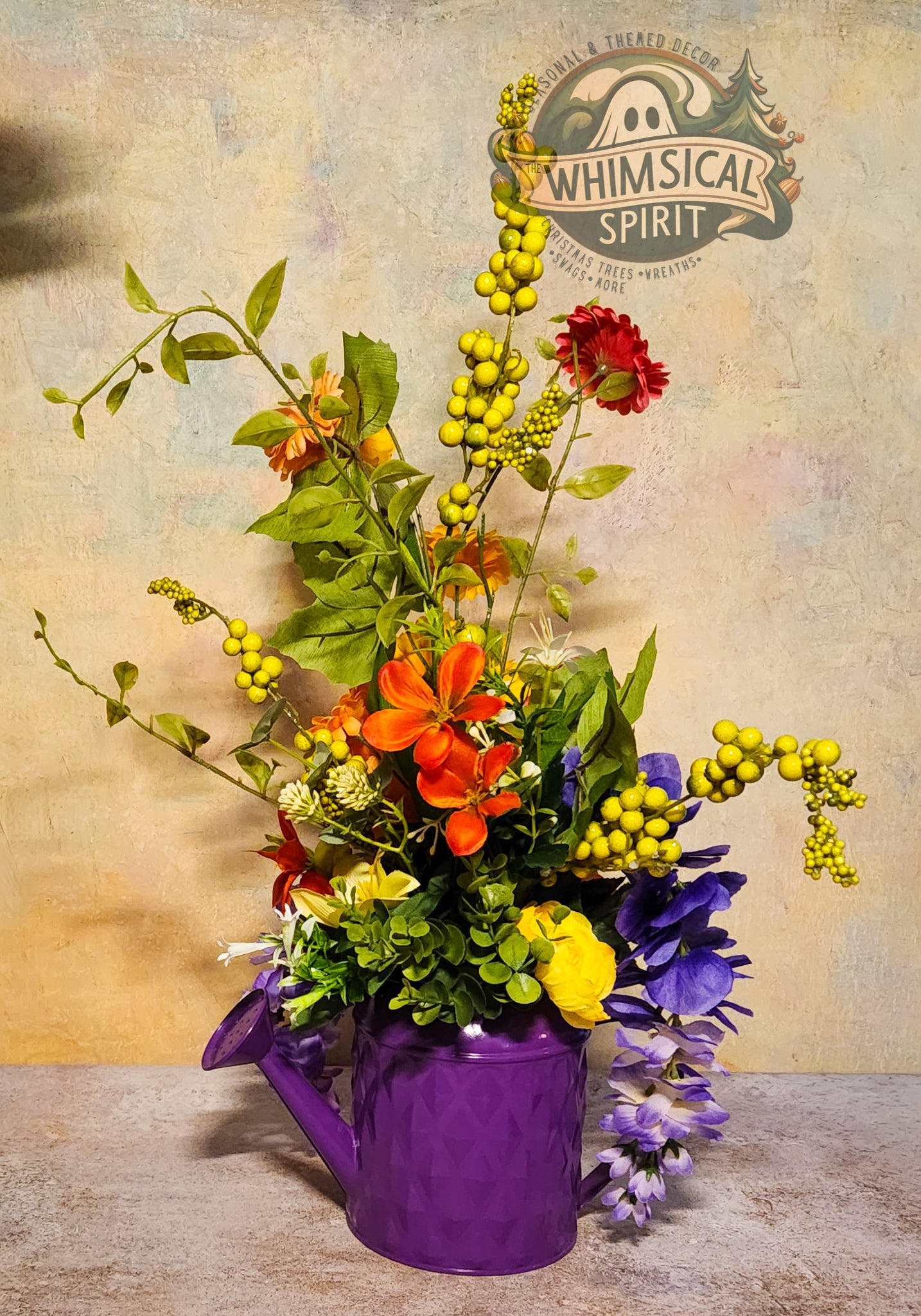 Colorful bouquet in a purple watering can with 'Whimsical Spirit' logo in the background