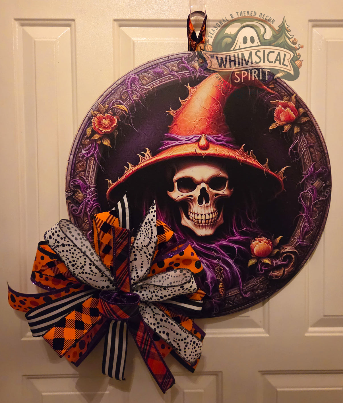 Round skeleton witch Halloween door hanger with an orange hat, ornate purple frame, antique roses, and a large patterned bow.