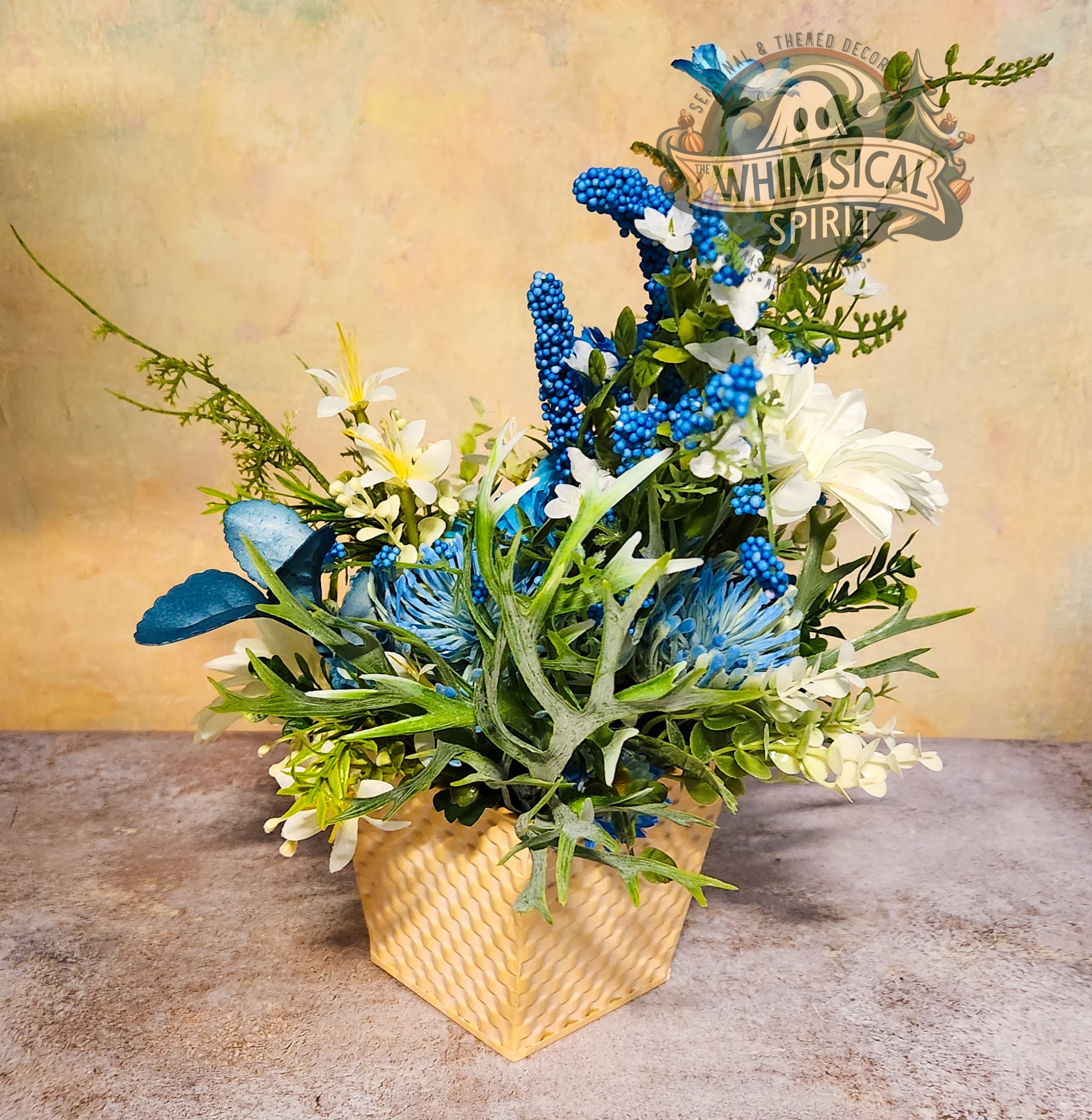 Decorative floral arrangement with blue and green elements in a woven basket on a textured surface.