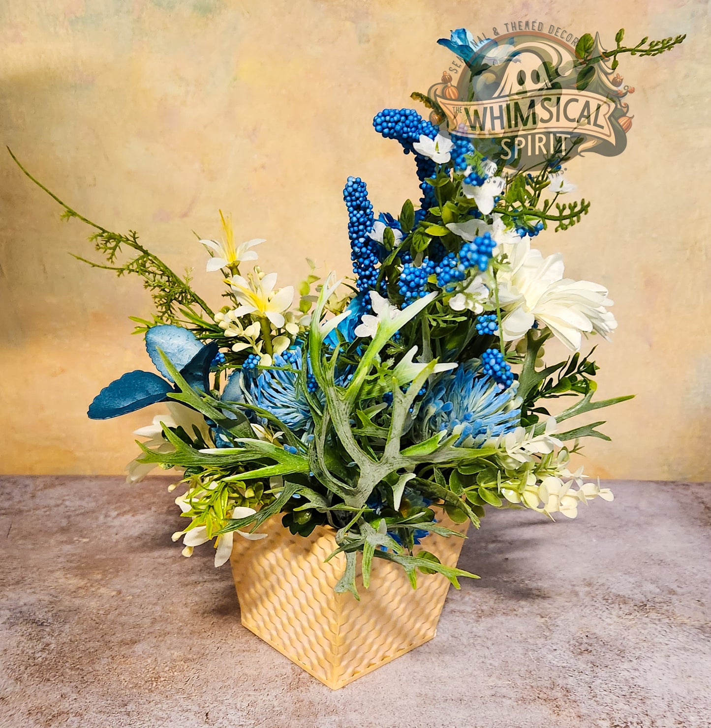 Decorative floral arrangement with blue and green elements in a woven basket on a textured surface.