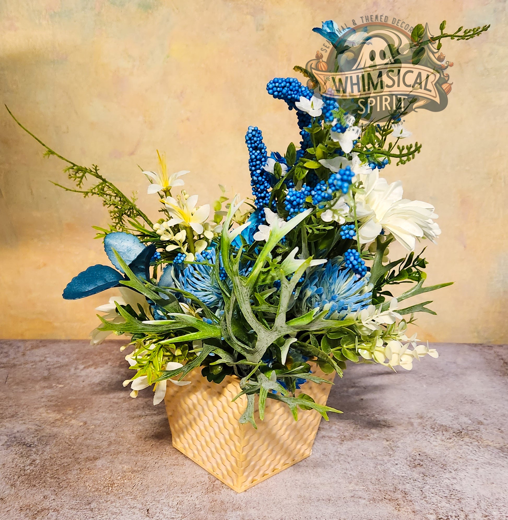 Decorative floral arrangement with blue and green elements in a woven basket on a textured surface.
