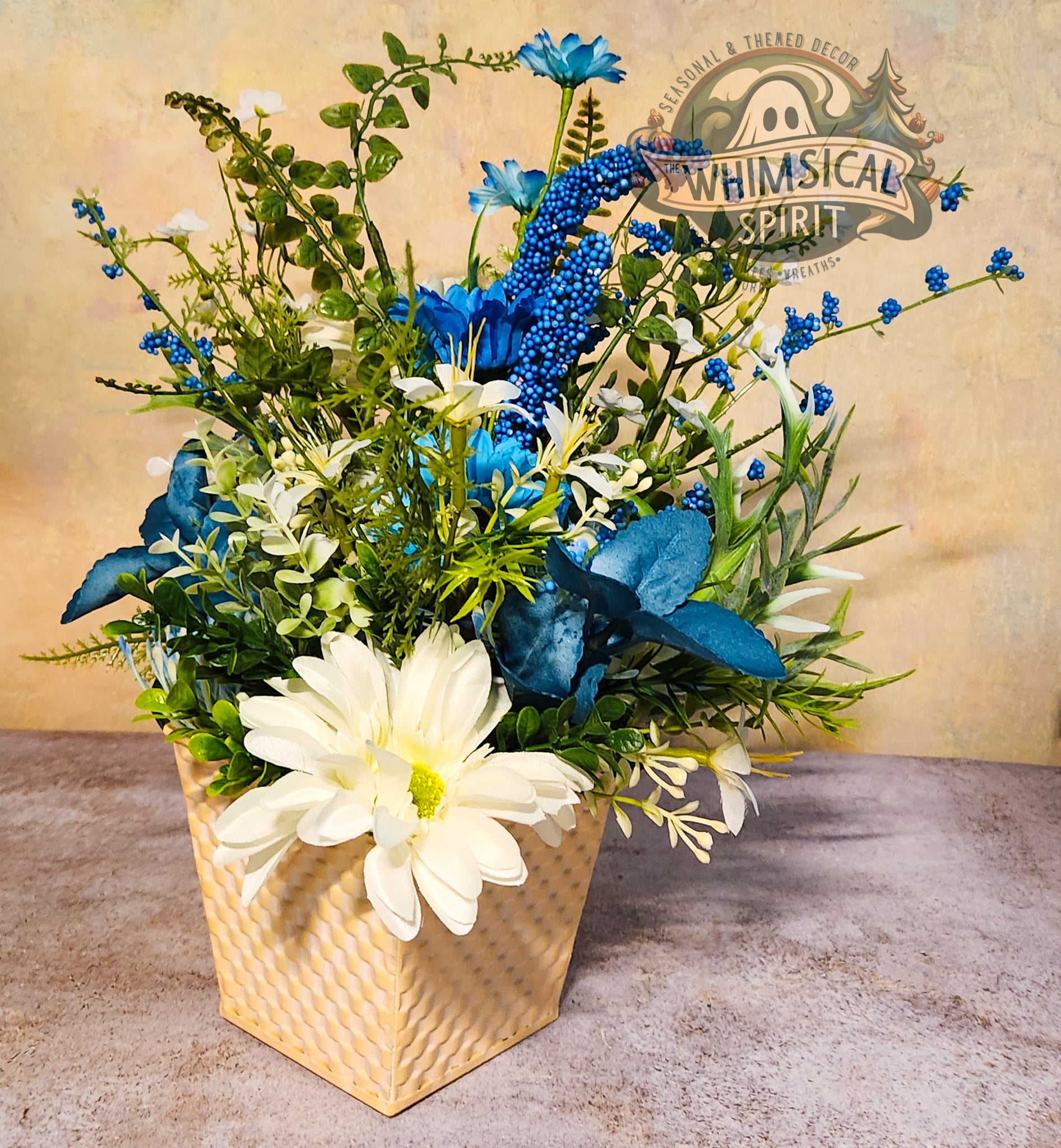 Floral arrangement with blue and white flowers in a woven basket on a textured surface, branded 'Whimsical Spirit'.