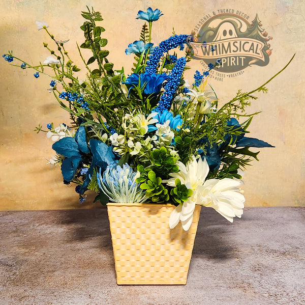 Floral arrangement in a yellow woven pot with 'Whimsical Spirit' branding in the background.
