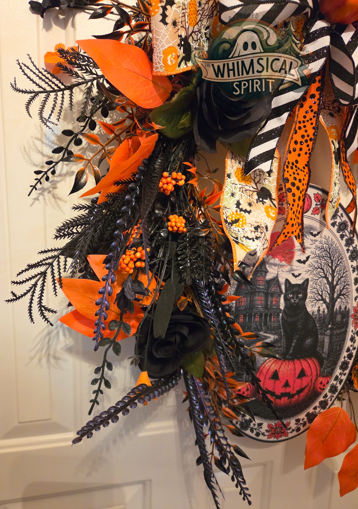 Halloween-themed decorative wreath with pumpkins, cats, and autumn leaves on a white door.
