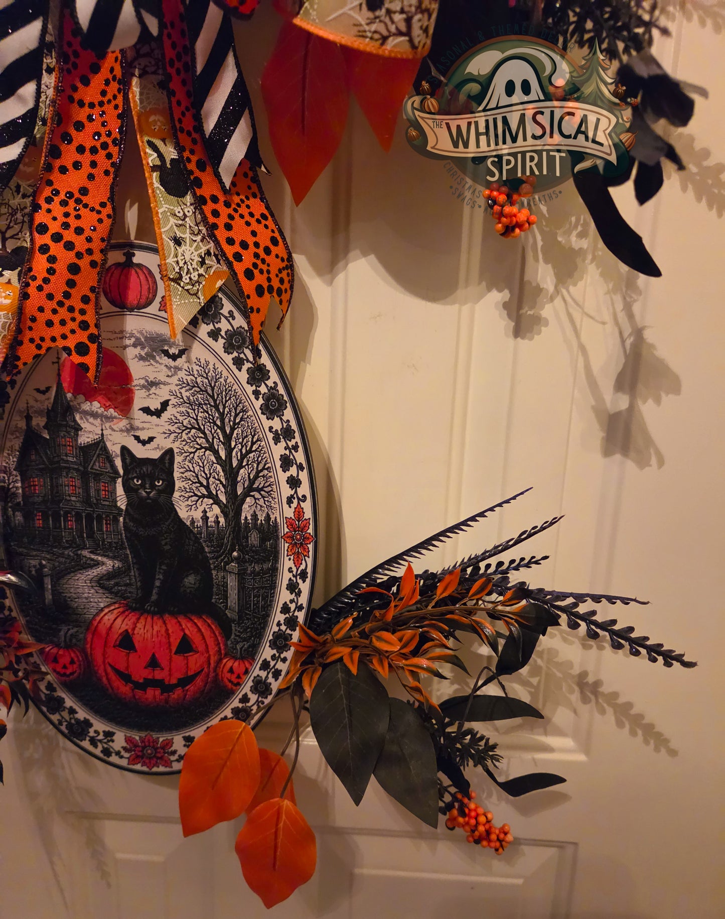 Decorative Halloween wreath with pumpkins, cats, and leaves on a white door.