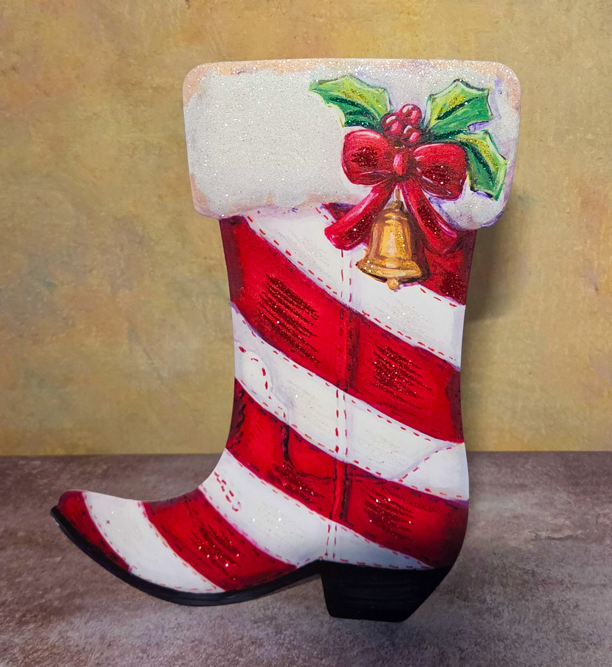 Front view of the Candy Cane Bell Boot with red-and-white stripes, a snowy cuff, holly, a red bow, and a gold bell.