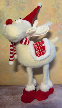 Front view of large white standing Christmas reindeer with a red nose, tall antlers, solid red Santa hat, striped scarf, patterned saddle, and plush red shoes.