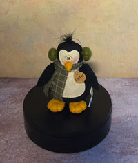 Front view of Parker penguin soft sculpture with green earmuffs, plaid scarf, golden feet, and name tag.