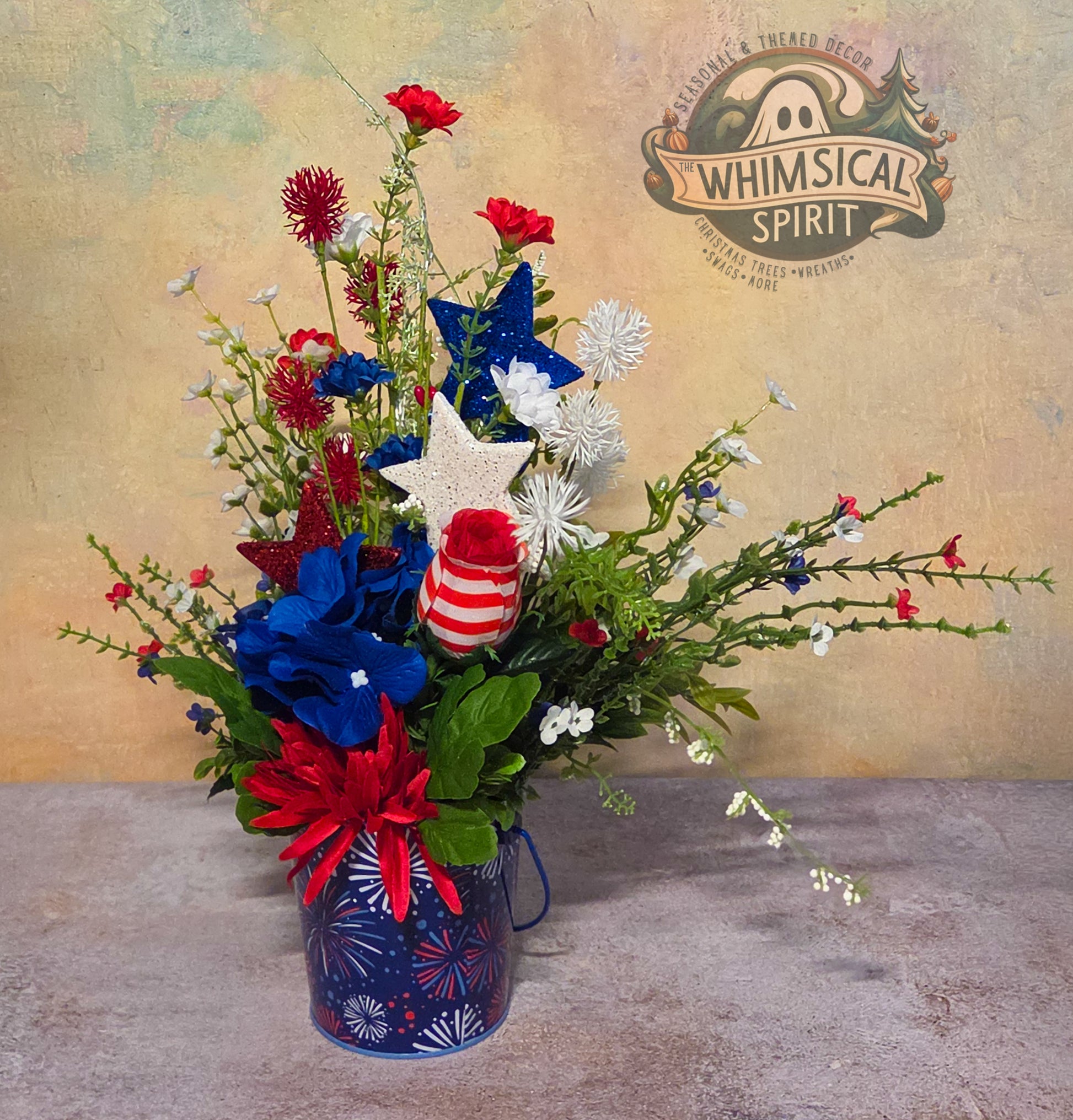 Floral arrangement with patriotic elements in a blue vase on a textured surface, featuring the 'Whimsical Spirit' brand.