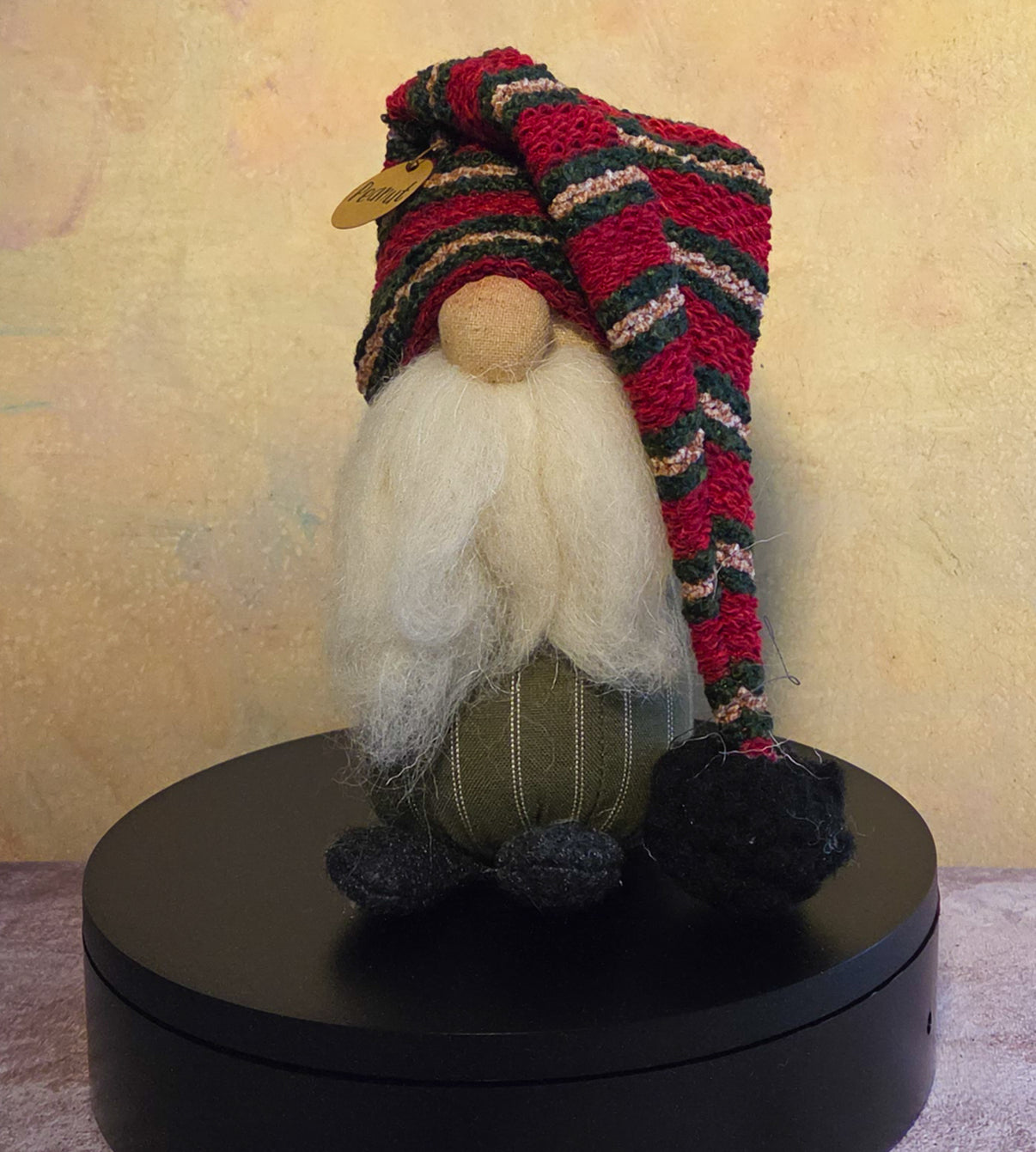 Peanut the Gnome winter soft sculpture shelf sitter with white beard, red and green striped knit hat, green fabric body, dark feet, and name tag.