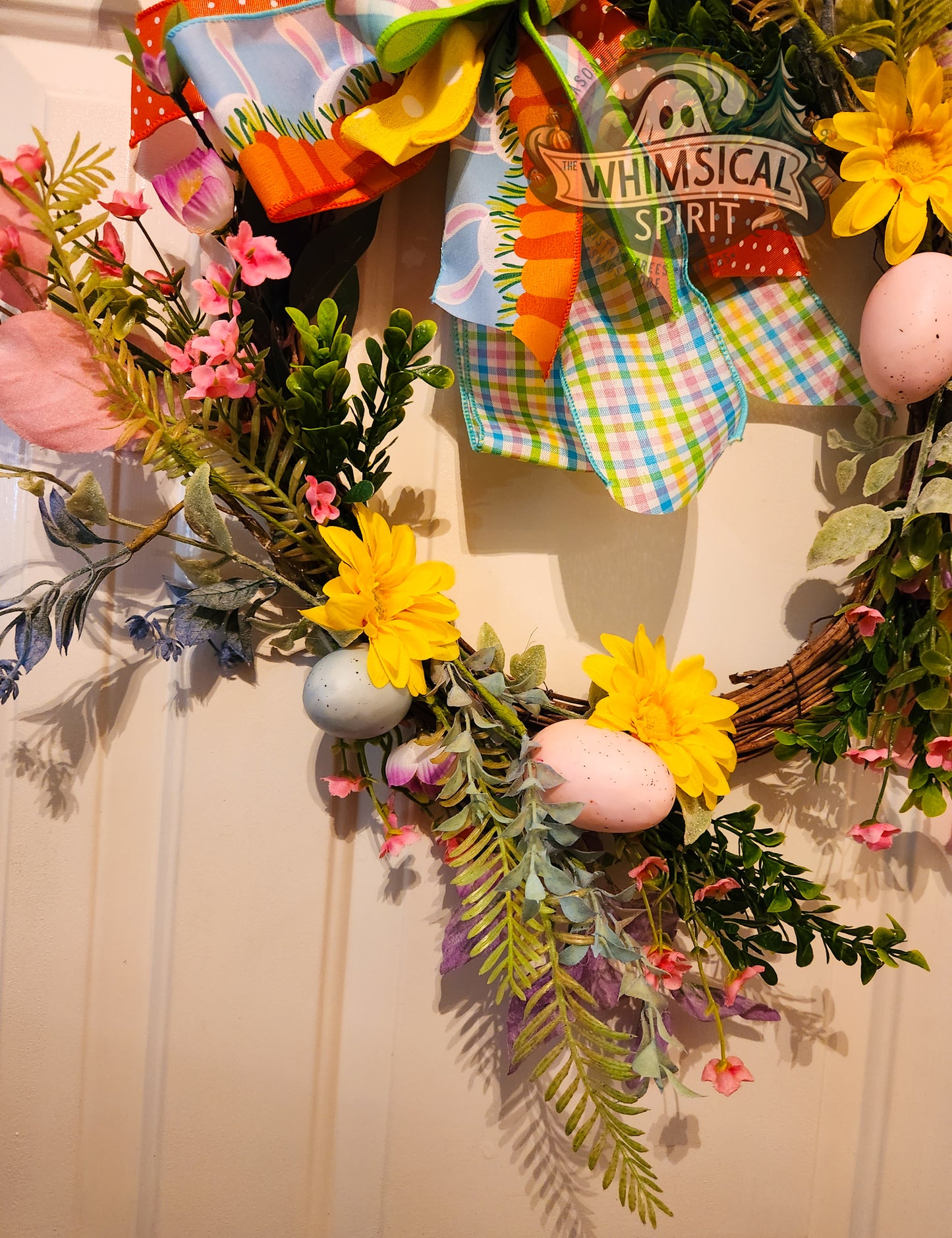 Decorative wreath with flowers, eggs, and a sign reading 'Whimsical Spirit' on a plain background.