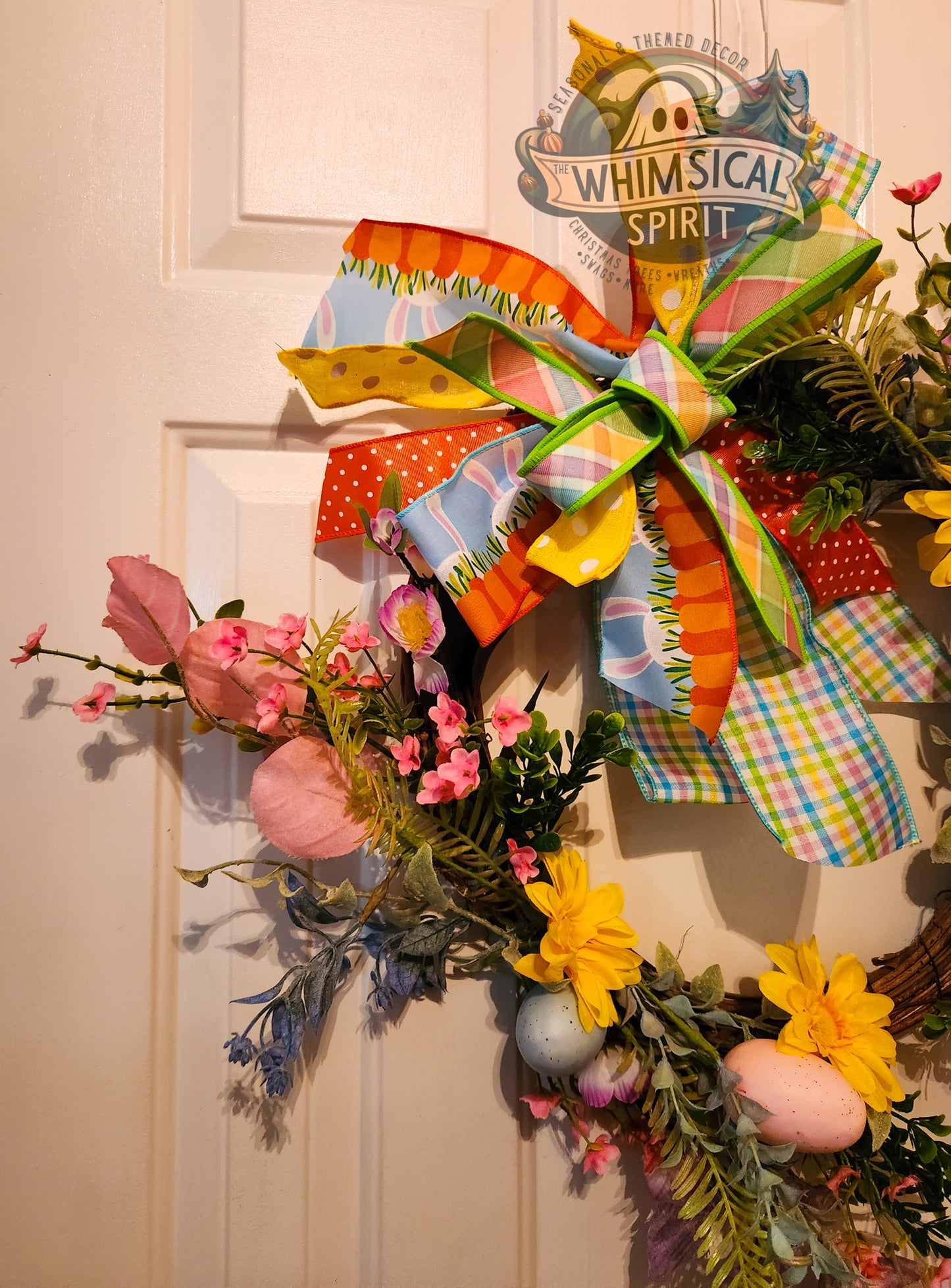 Decorative wreath with colorful bow and flowers on a door, featuring 'Whimsical Spirit' branding.