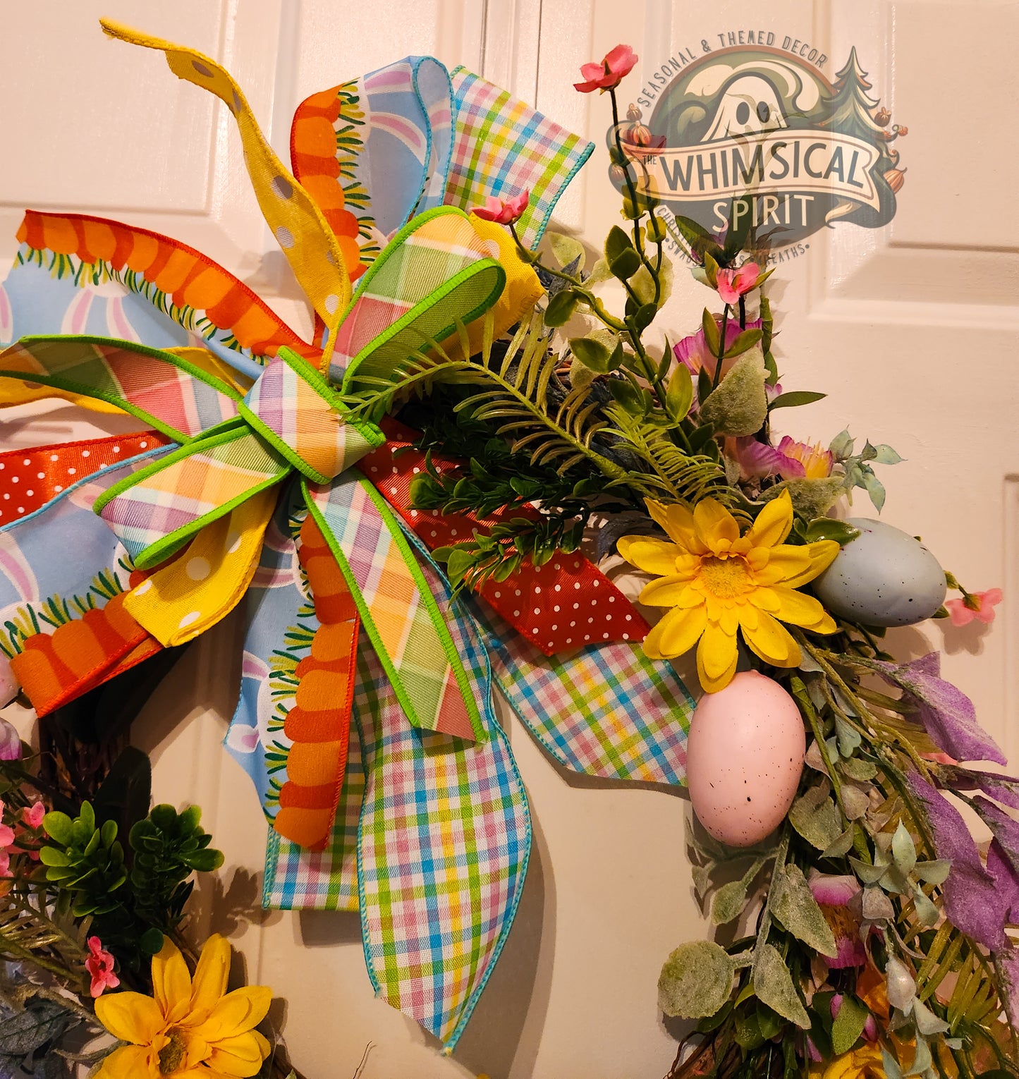 Colorful Easter wreath with eggs and flowers on a door, featuring 'Whimsical Spirit' branding.