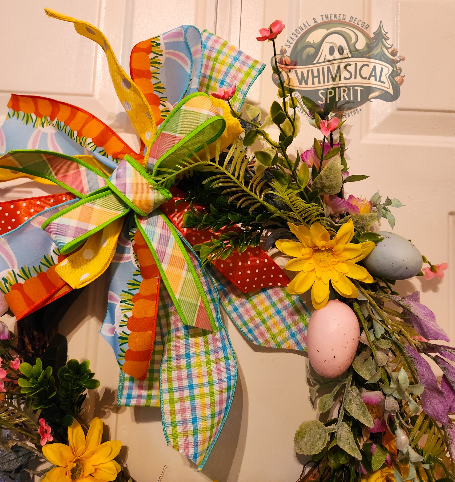 Colorful Easter wreath with eggs and flowers on a door, featuring 'Whimsical Spirit' branding.