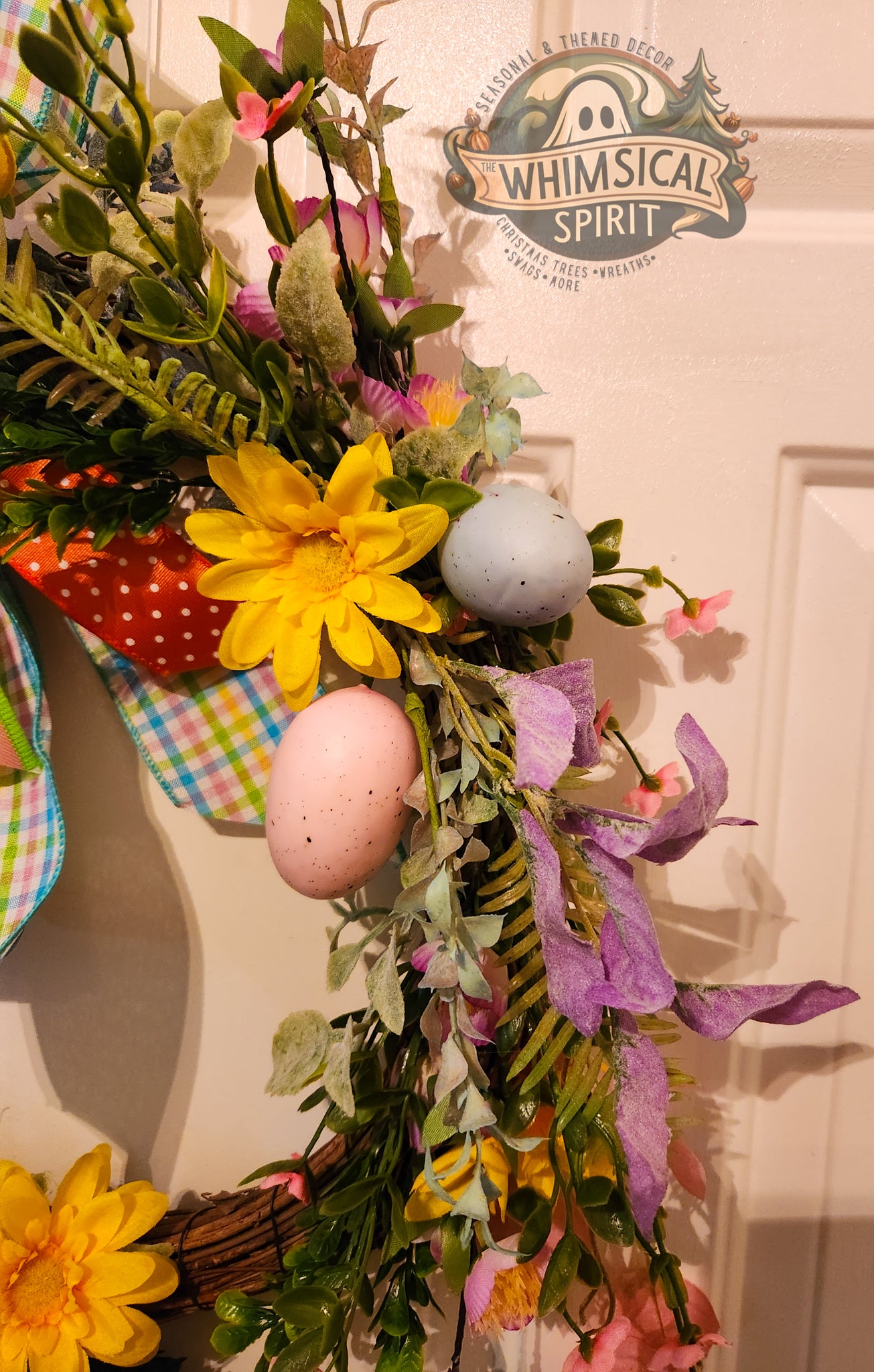 Decorative Easter wreath with eggs and flowers on a door, featuring 'Whimsical Spirit' branding.