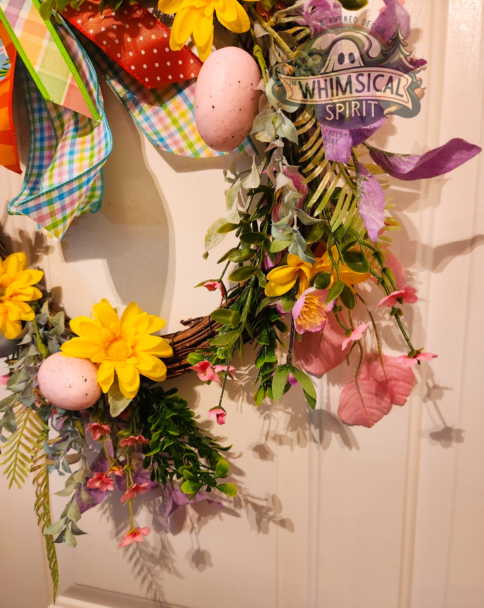 Decorative wreath with flowers, eggs, and a 'Whimsical Spirit' sign on a white door.