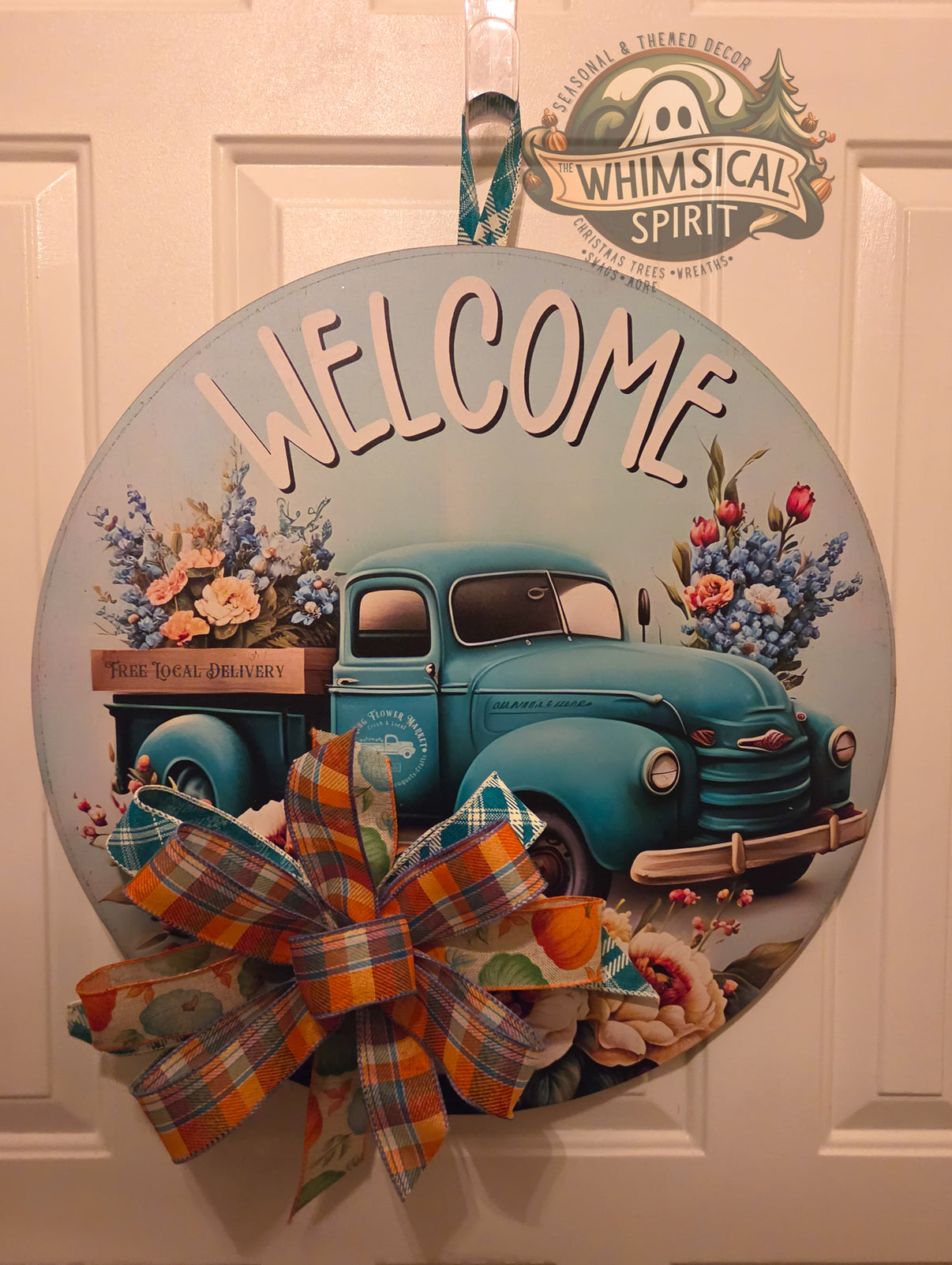 Round welcome door hanger with a vintage teal flower truck, soft blue background, floral details, and an orange-and-teal plaid bow.