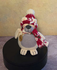 Front view of Pheby polar bear soft sculpture wearing a red and cream knit hat and scarf with a gray belly and wooden name tag.
