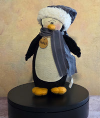 Prince the Penguin winter soft sculpture shelf sitter with gray scarf, plaid winter hat, plush black-and-white penguin body, and name tag.