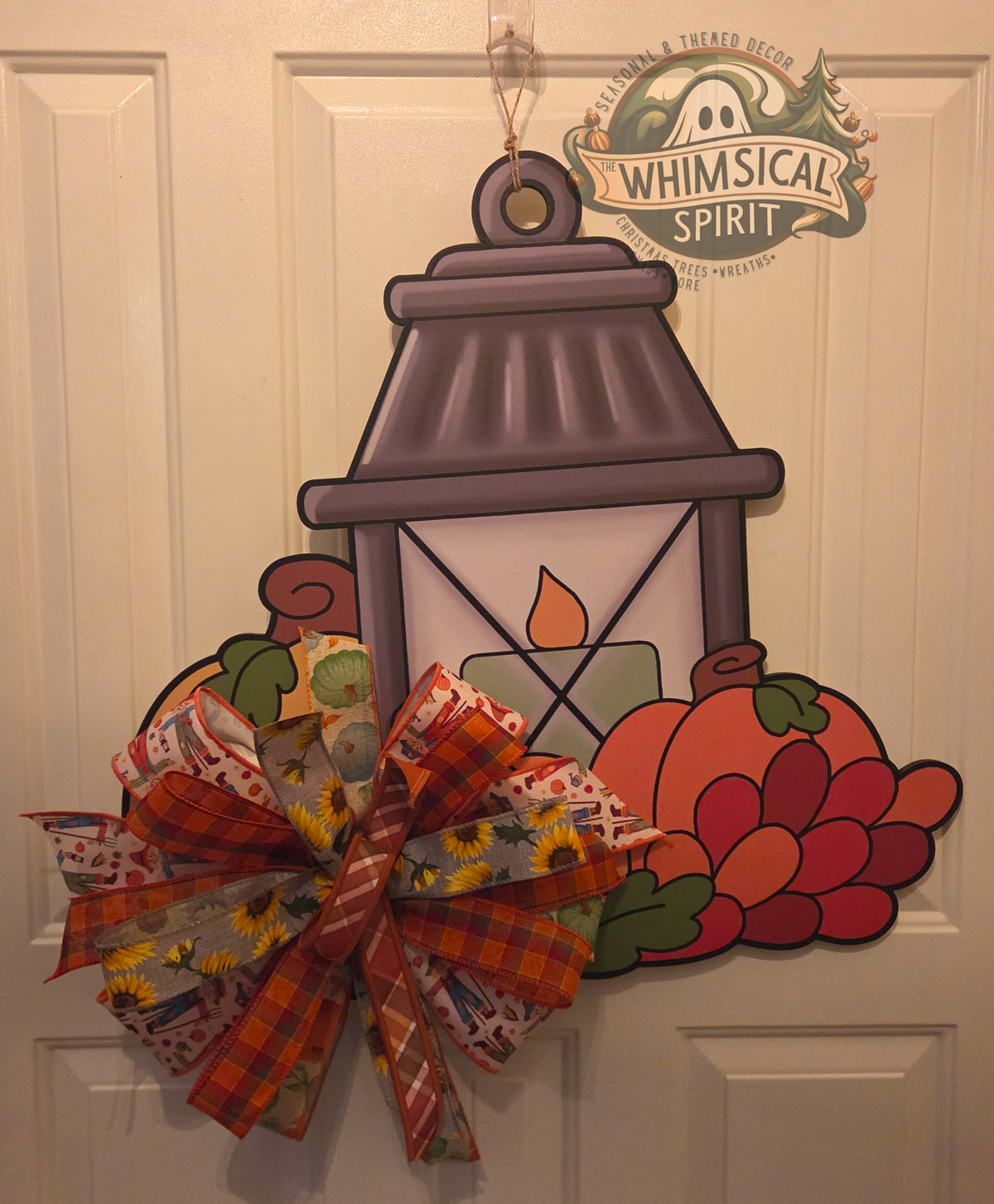 Pumpkin Glow fall birch wood door hanger with a lantern, pumpkins, berries, and large sunflower plaid bow on a white door.