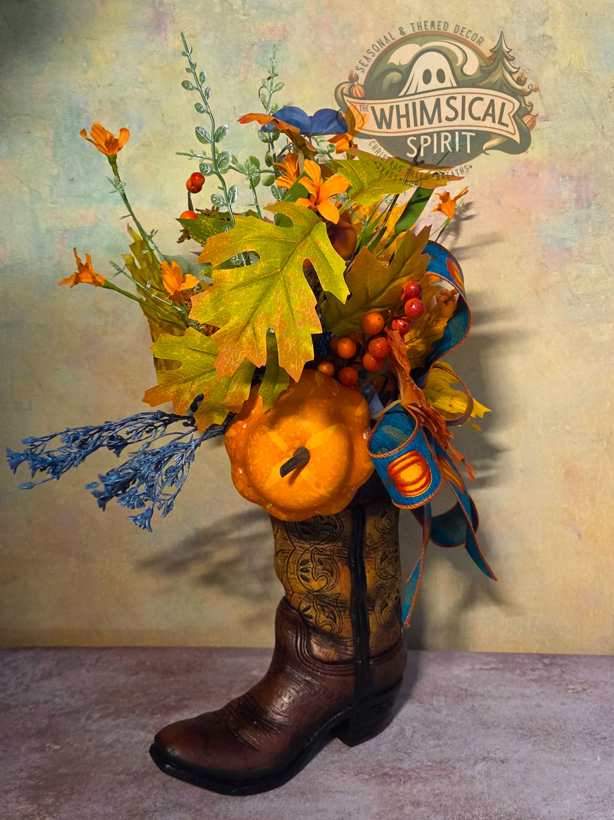 Handmade fall centerpiece in a brown cowboy boot with an orange pumpkin, berries, autumn leaves, and teal ribbon.