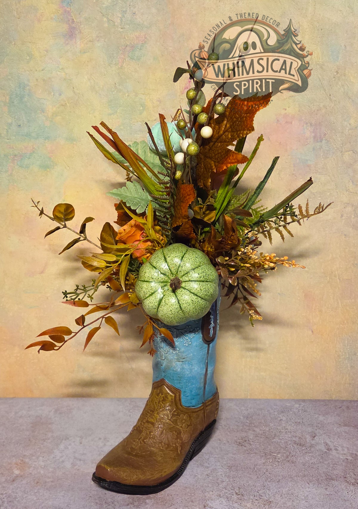 Blue and brown cowboy boot fall centerpiece with a sage-green pumpkin, autumn foliage, grasses, ferns, and berry branches.