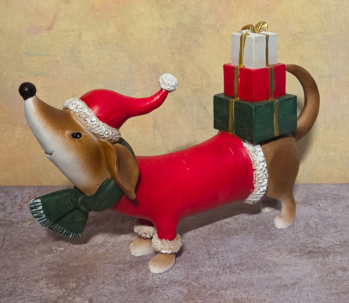 Large Christmas dog figurine wearing a red Santa suit, green scarf, and Santa hat with three wrapped presents balanced on its back.