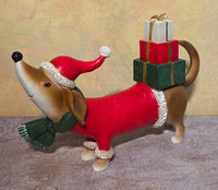 Large Christmas dog figurine wearing a red Santa suit, green scarf, and Santa hat with three wrapped presents balanced on its back.