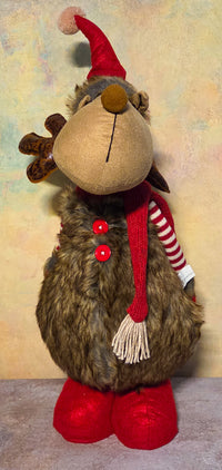 A Christmas reindeer plush toy with brown faux fur, a red Santa hat, a red and white striped scarf, and red boots, set against a textured beige background.